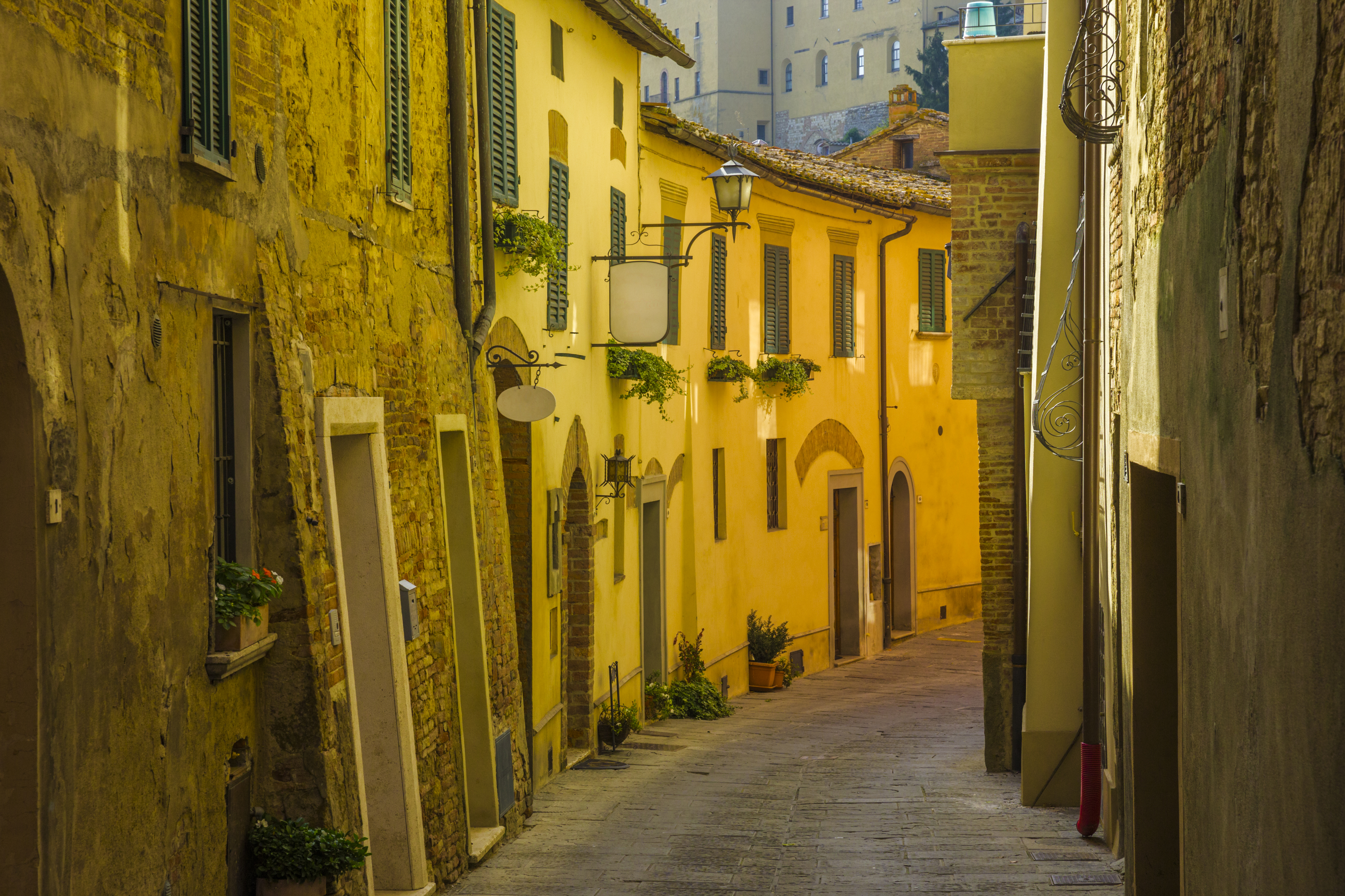 Narrow shady street with yellow golden stone buildings with small windows in Montepulciano Tuscany