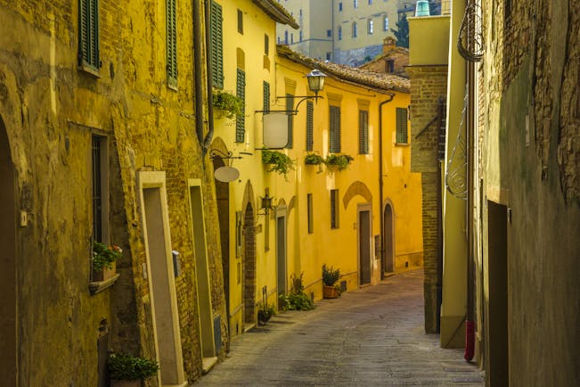 Narrow shady street with yellow golden stone buildings with small windows in Montepulciano Tuscany