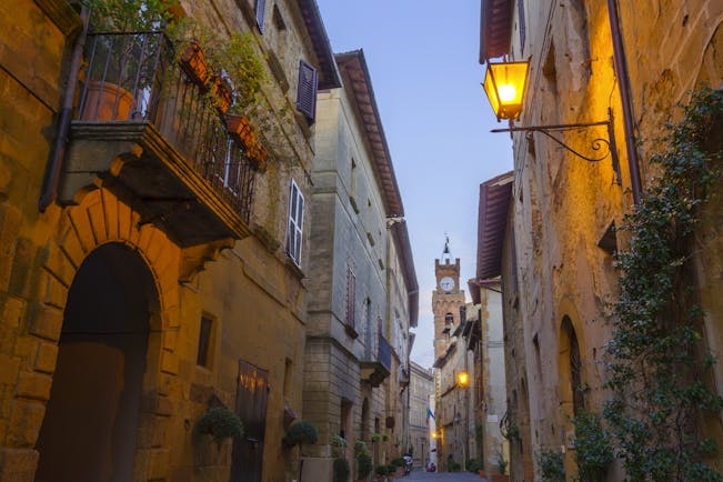 Narrow street at dusk with lamps on sides of houses in Pienza Tuscany