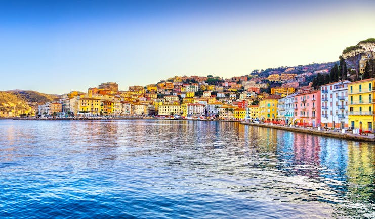 Houses pained blue, yellow and pink lining the calm seashore at Porto Santo Stefano on the Argentario in Tuscany