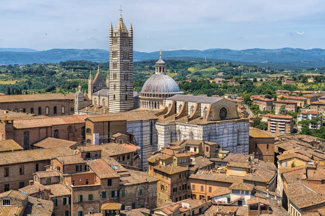 Terracotta roofs of historic houses in Siena with the dome and tower of the cathedral