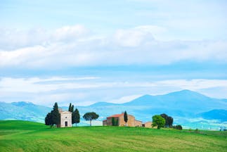 Tuscany field with small white chapel flanked by cypress trees with mountains behind