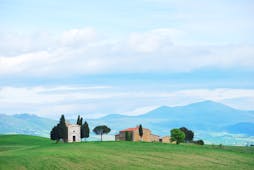 Tuscany field with small white chapel flanked by cypress trees with mountains behind