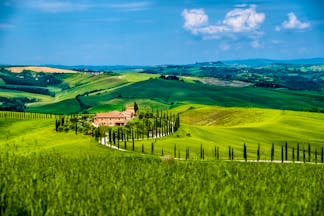 Green hills with cypress trees and orange coloured farmhouse in Tuscany