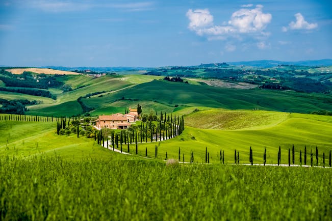 Green hills with cypress trees and orange coloured farmhouse in Tuscany