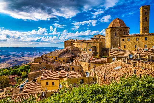 Dark golden stone houses on a hill with church dome and bright blue sky in Volterra Tuscany