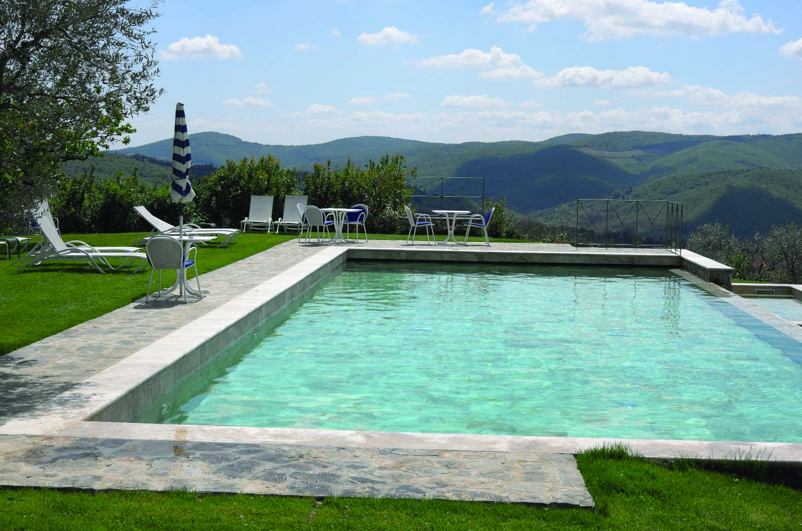 View of the infinity pool with white sunbeds around looking over the grassy mountains 