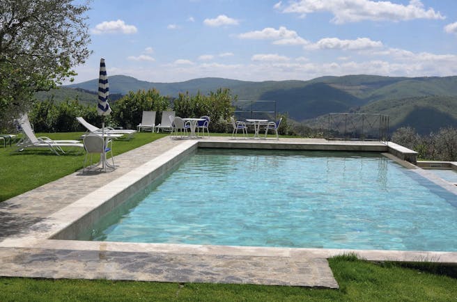 View of the infinity pool with white sunbeds around looking over the grassy mountains 