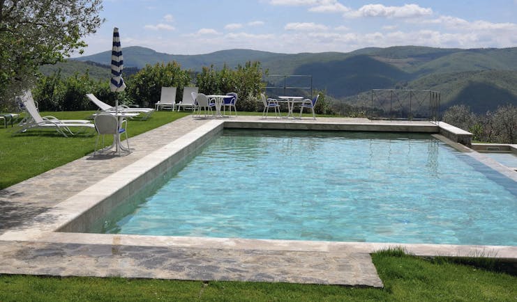 View of the infinity pool with white sunbeds around looking over the grassy mountains 