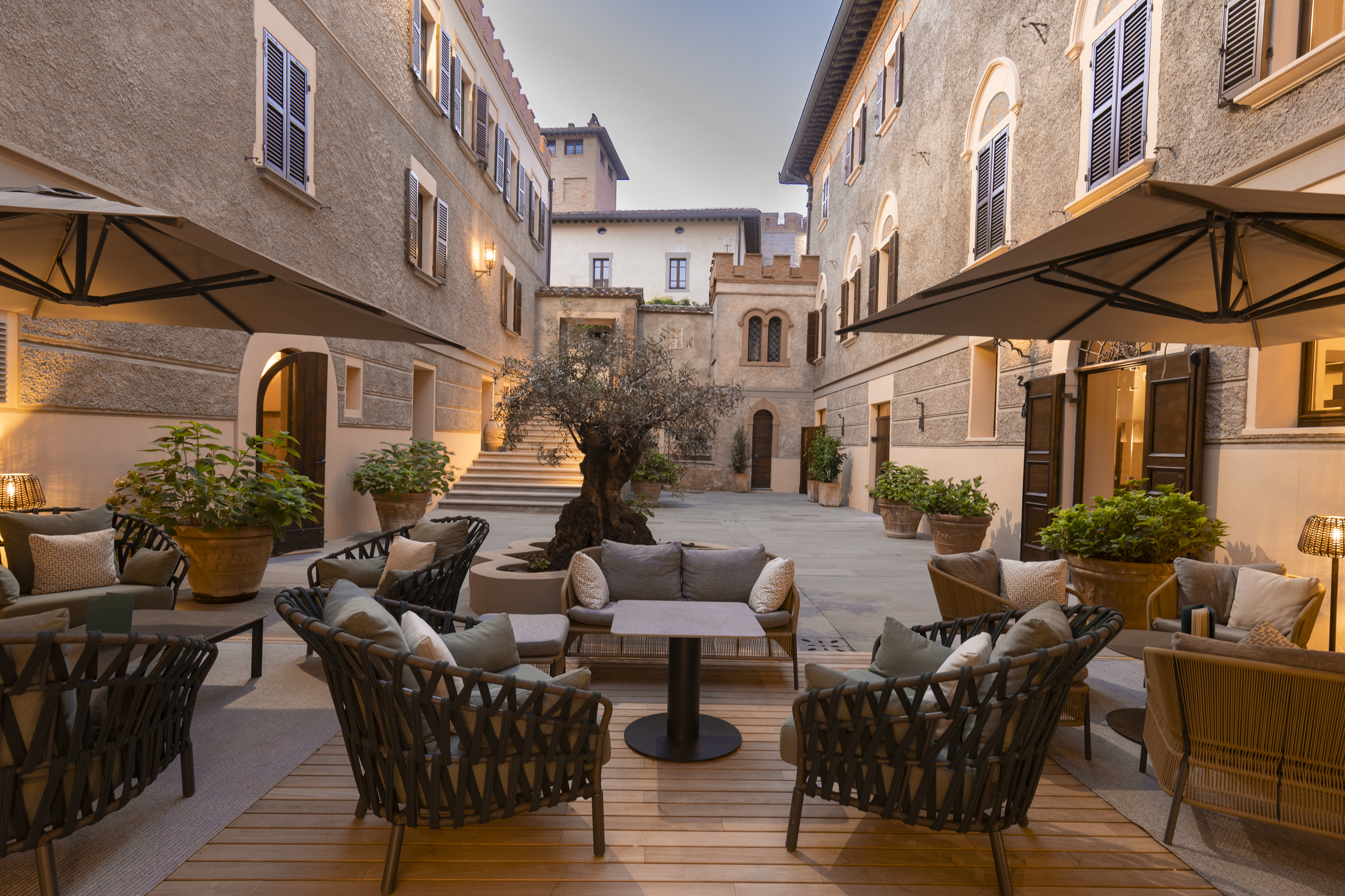 Borgo dei Conti bar in the inner courtyard, with rattan chairs and plush sofas, interspersed with shrubs and parasols, and the hotel's stone buildings on either side