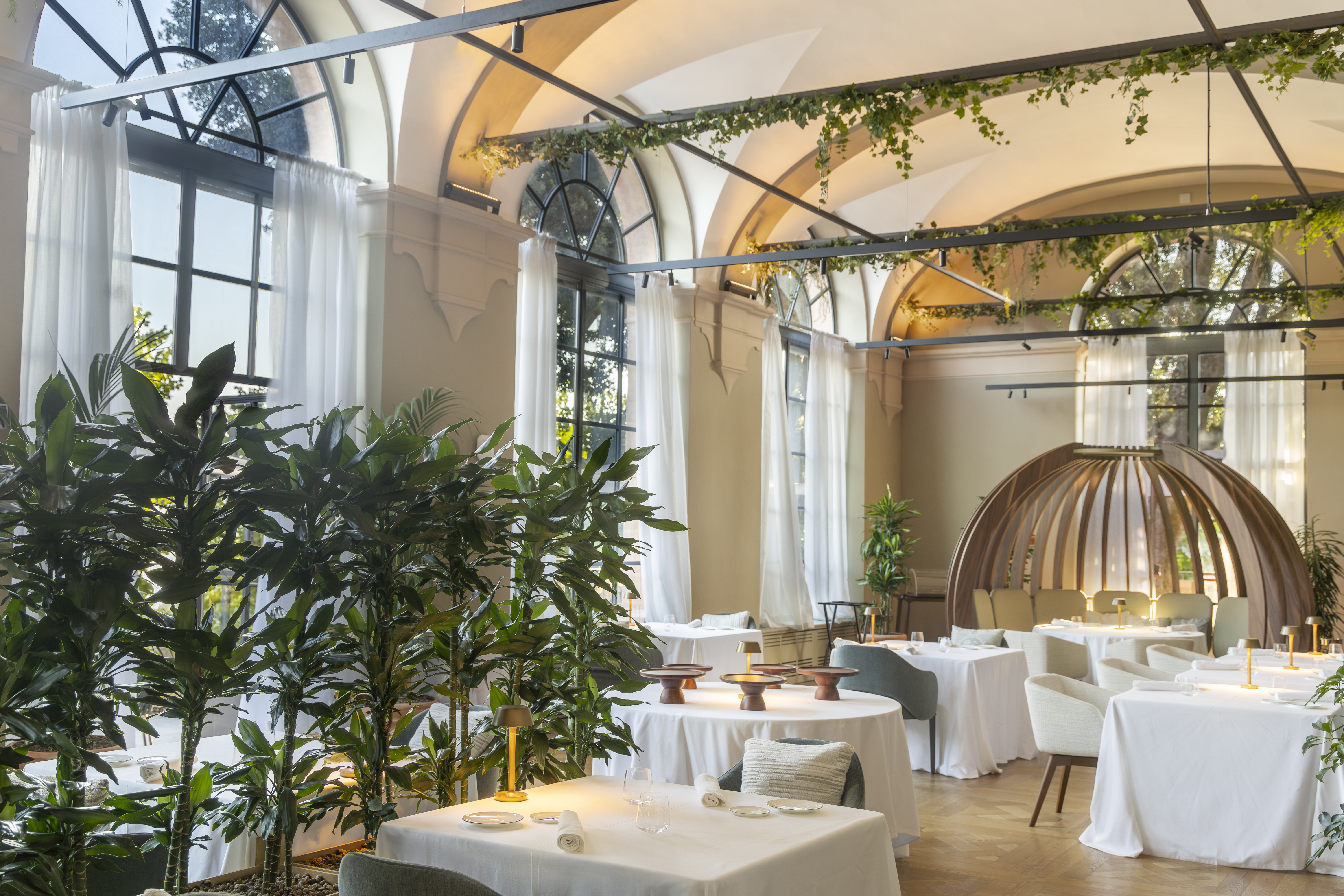 Borgo dei Conti Cedri Restaurant, with floor-to-ceiling arched windows, vines winding across iron beams, and arched ceiling