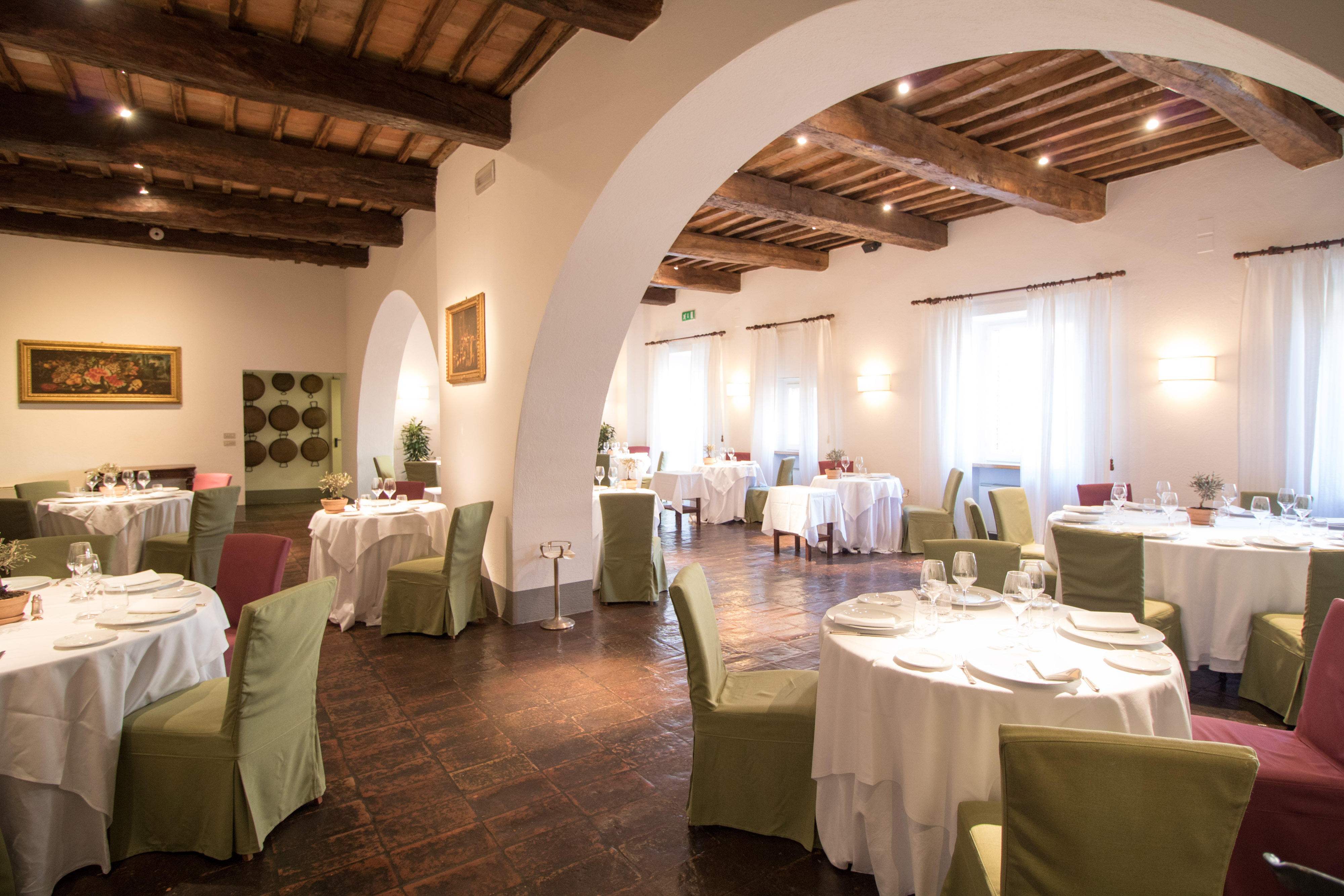 Large restaurant with white arched ceiling and round tables with green chairs