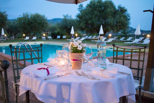Table set with white cloth and candles at side of pool in evening