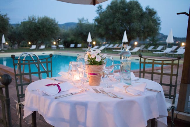 Table set with white cloth and candles at side of pool in evening