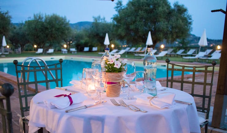 Table set with white cloth and candles at side of pool in evening