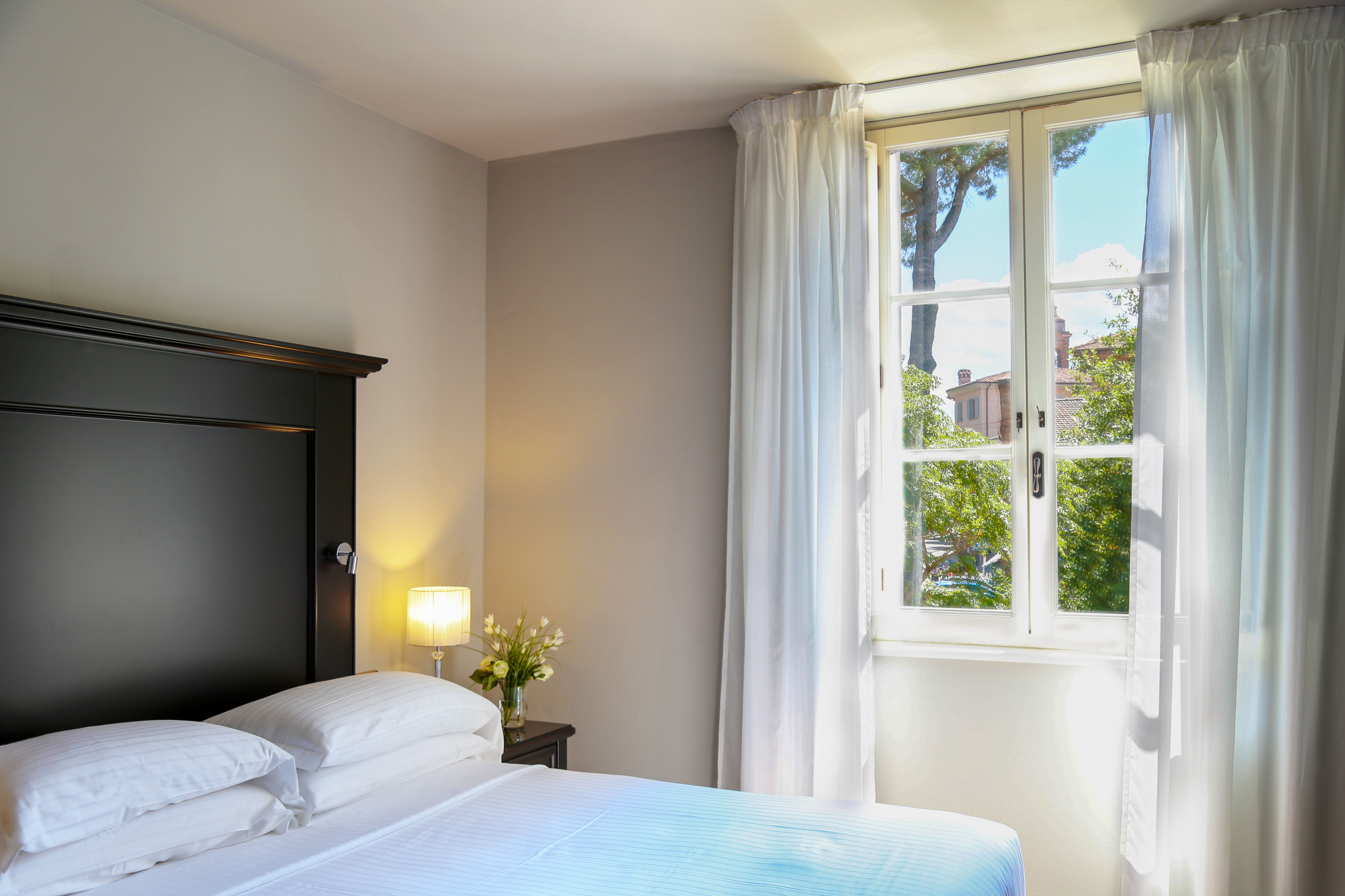 Hotel Vannucci Classic Room with dark bed frame, window looking out on the town, and white decor and linens