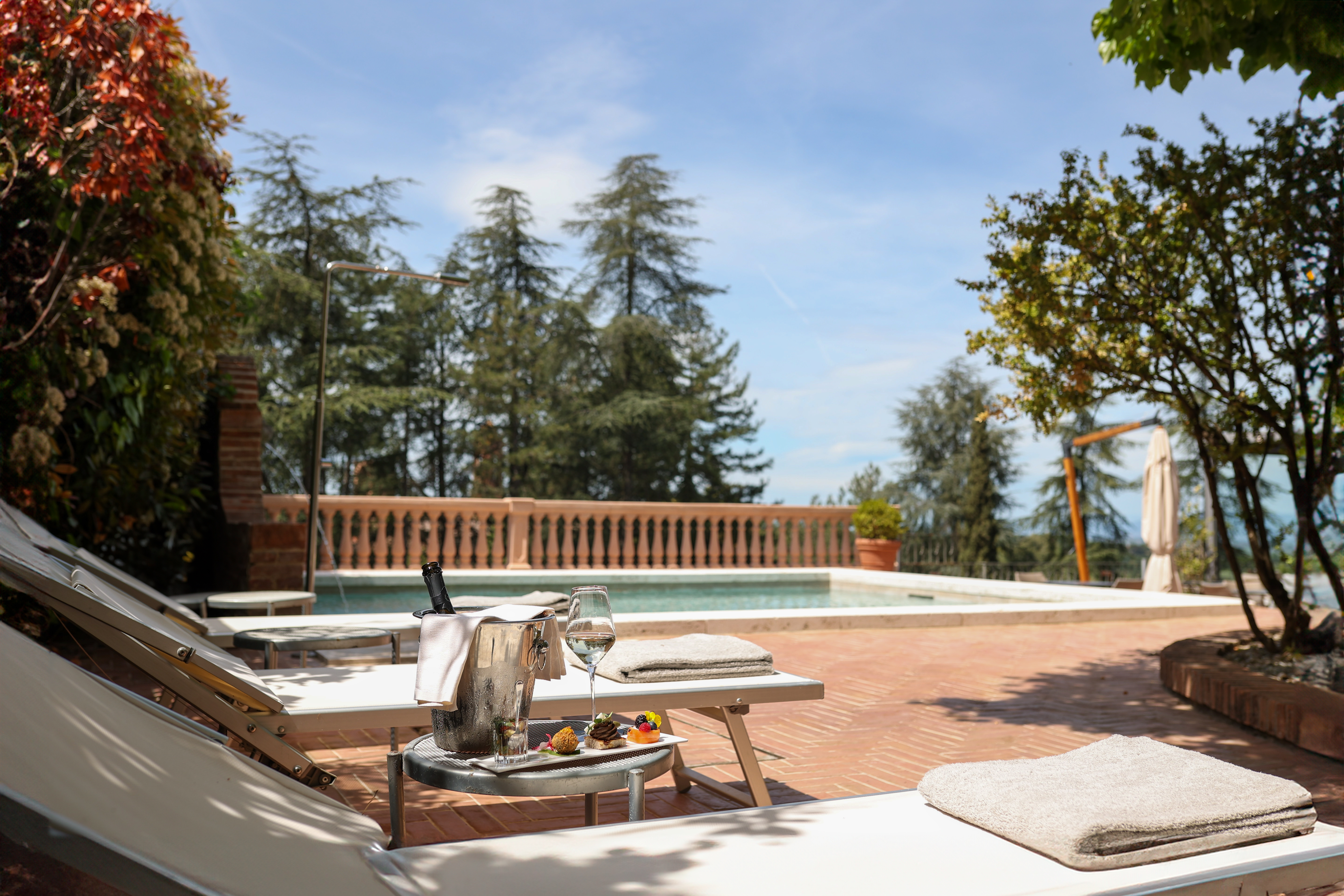 Hotel Vannucci poolside, with terracotta patio and white sun loungers shaded by trees
