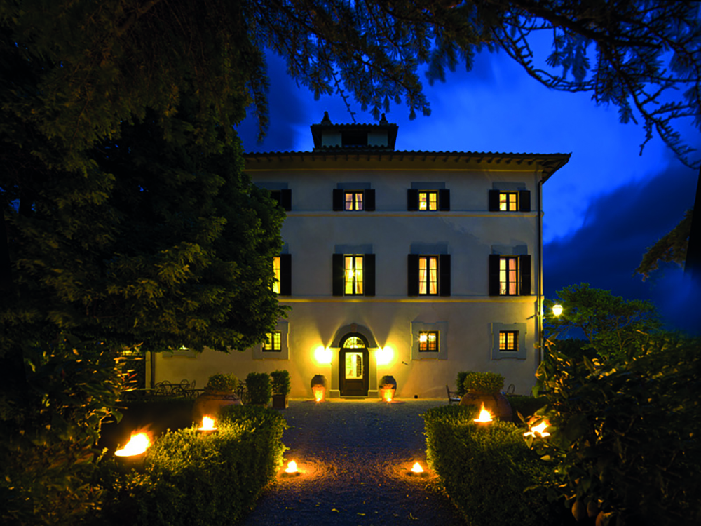 Hotel Villa di Monte Solare exterior at night, large white building with yellow rectangular windows with black shutters 