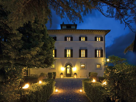 Hotel Villa di Monte Solare exterior at night, large white building with yellow rectangular windows with black shutters 