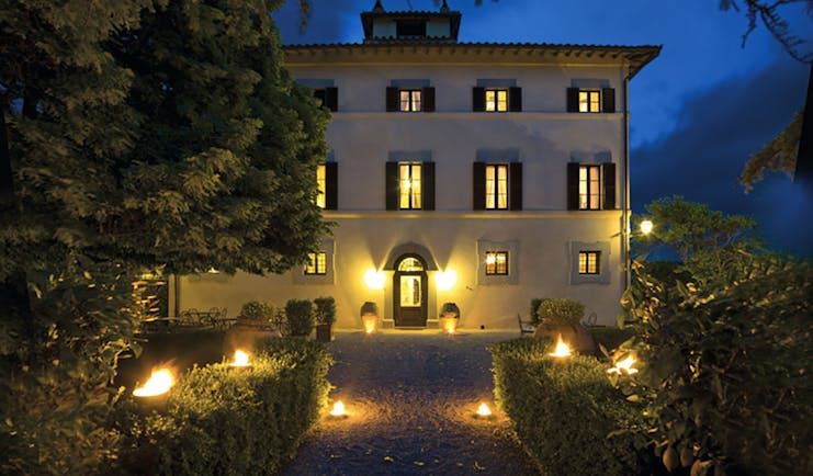 Hotel Villa di Monte Solare exterior at night, large white building with yellow rectangular windows with black shutters 
