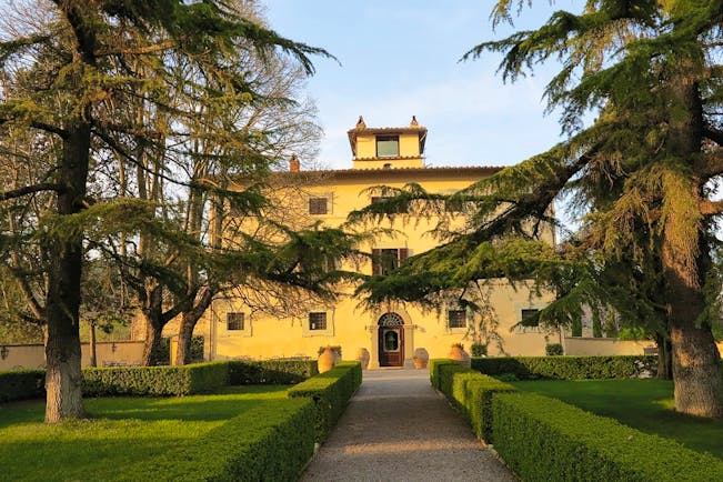 Exterior of hotel showing yellow building, freshly trimmed hedges and trees