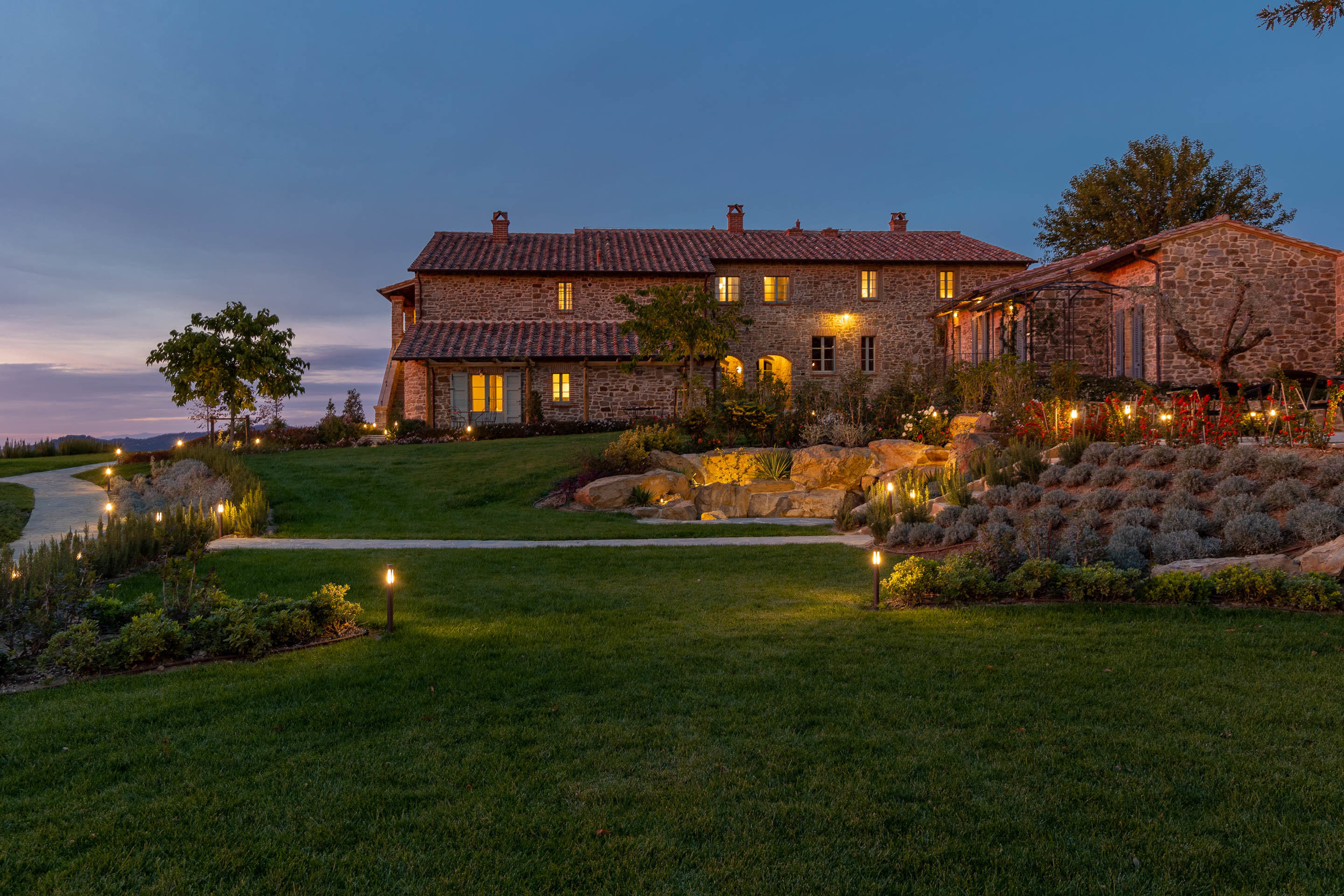 I Borghi Dell'Eremo at evening time, with warm lights glowing out of the stone building's windows and illuminating the paths winding around the hotel grounds
