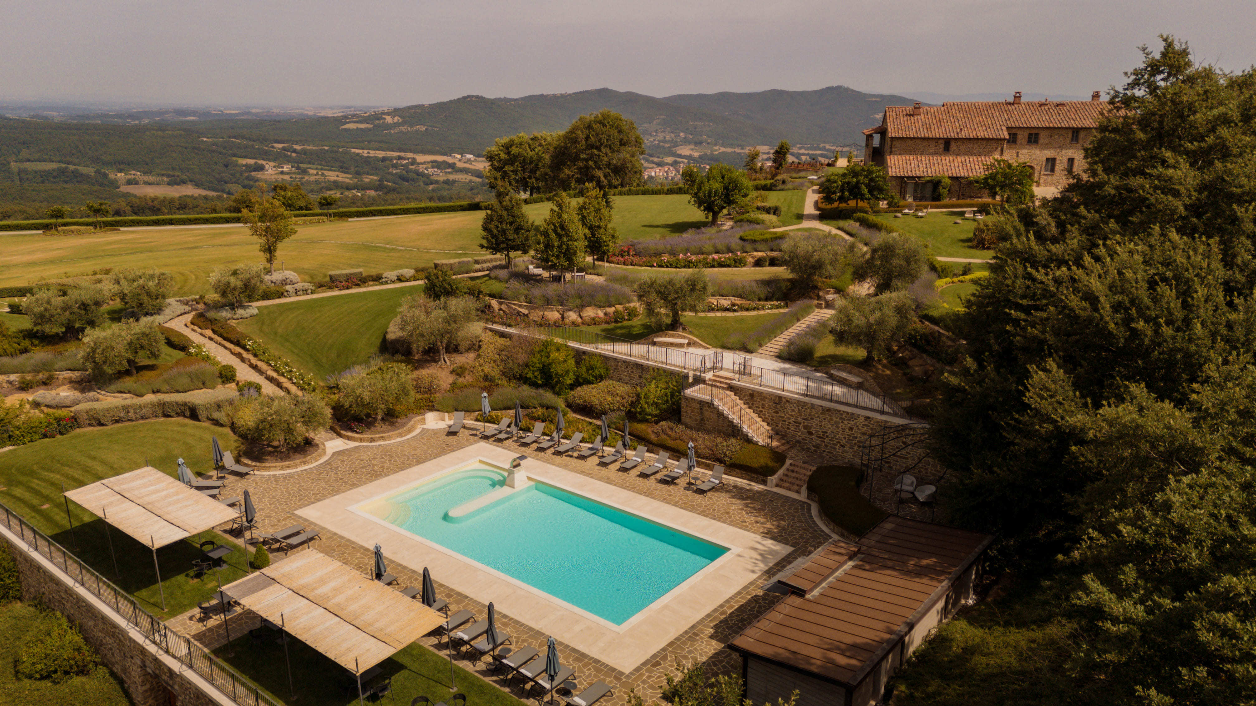 I Borghi Dell'Eremo poolside, with tiered gardens, ochre hotel building, and rolling Umbrian hills in the background