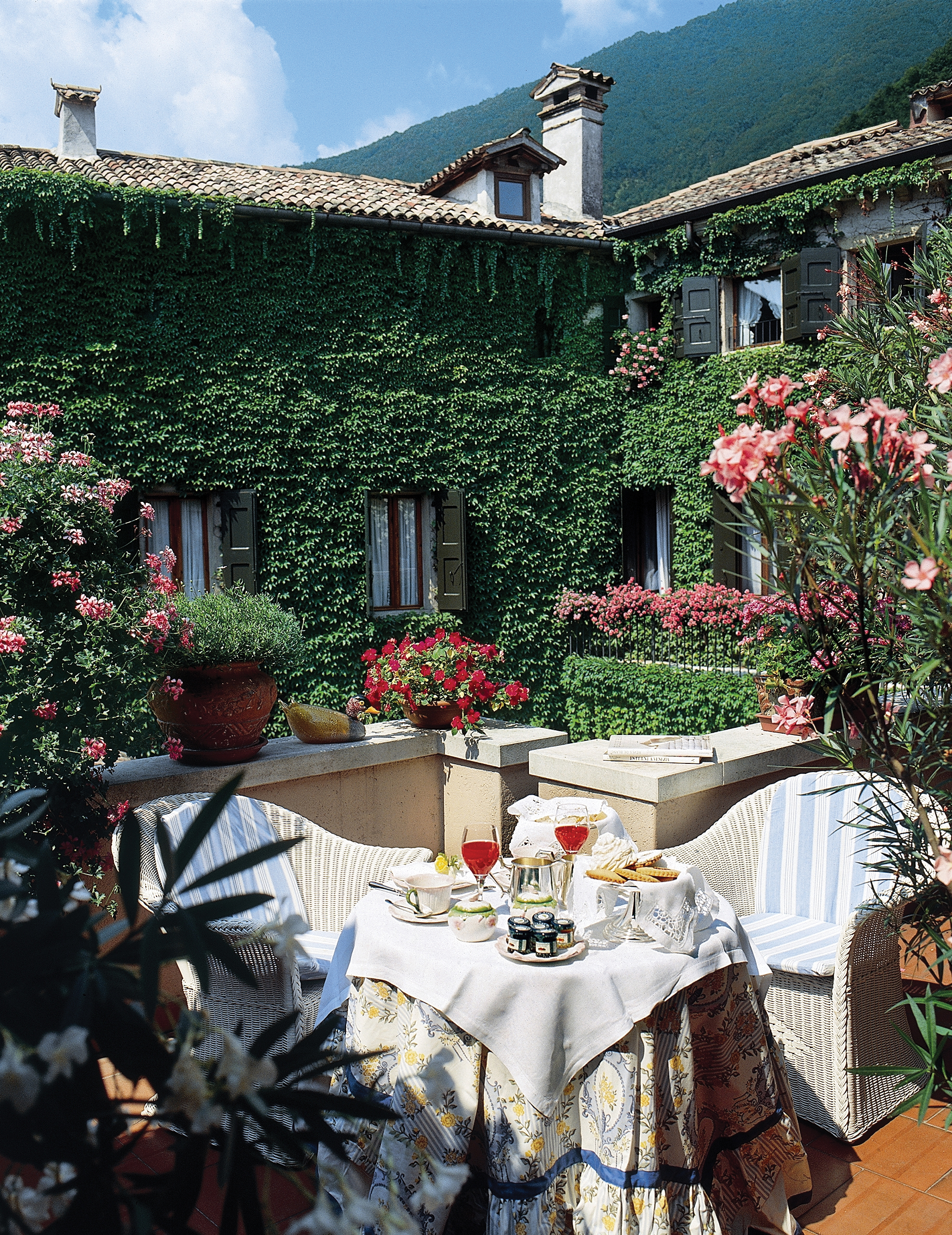 Hotel grounds with hotel building in the background covered in vines and tables and chairs set out with afternoon tea