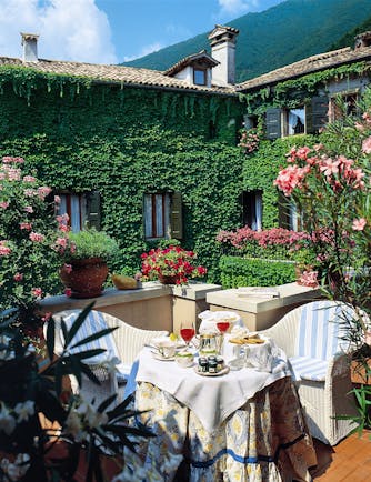 Hotel grounds with hotel building in the background covered in vines and tables and chairs set out with afternoon tea