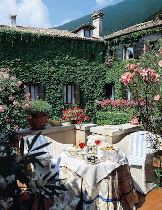 Hotel grounds with hotel building in the background covered in vines and tables and chairs set out with afternoon tea