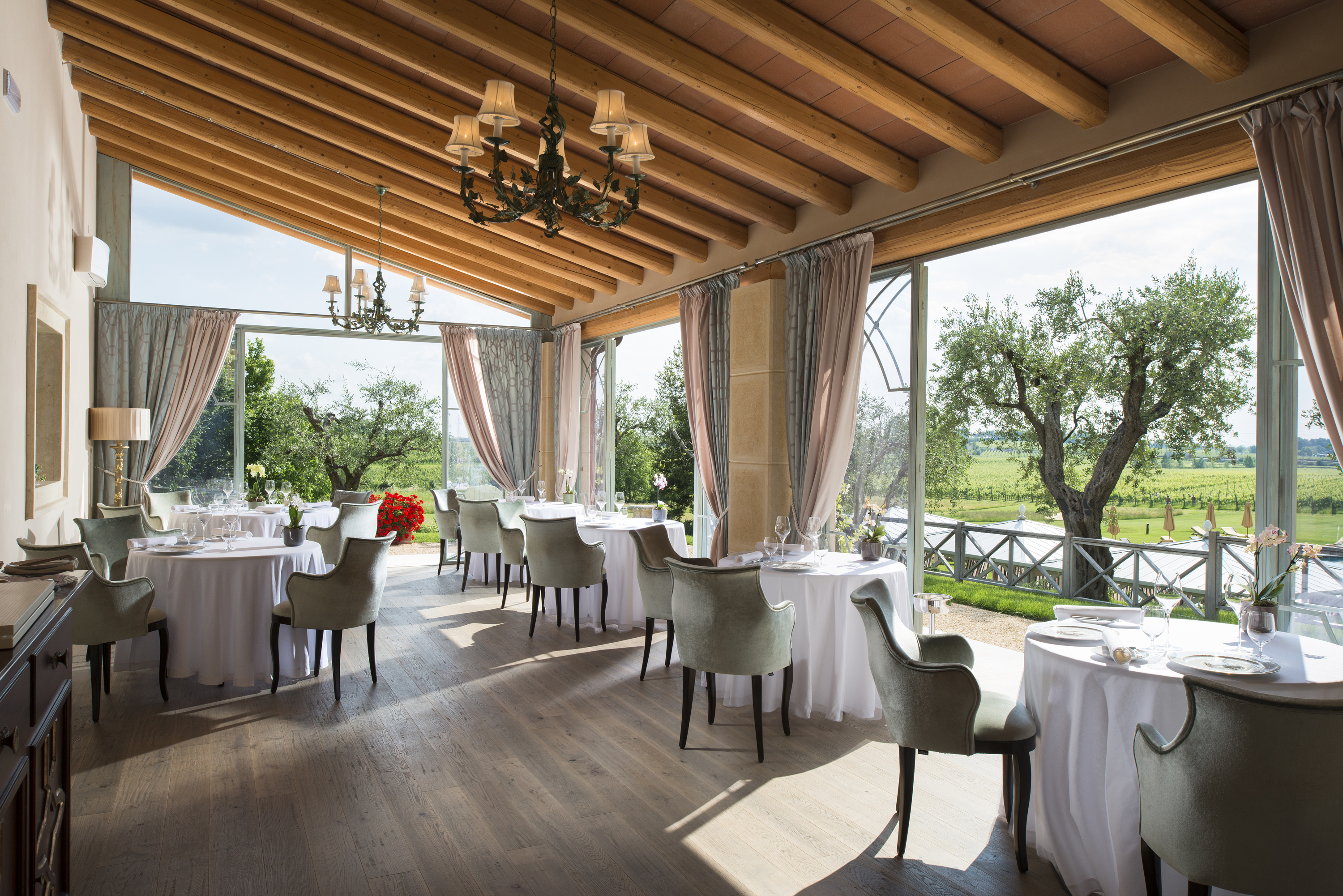 Villa Cordevigo dining room with white chairs and table cloths and a beamed ceiling, looking out over the gardens