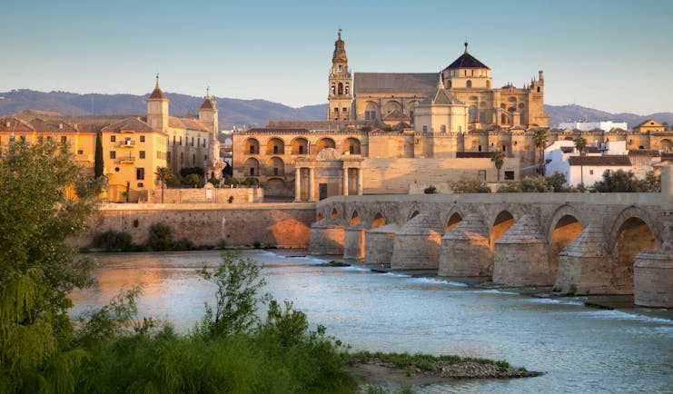Pink tinged sunlight on the Mezquita cathedral by the river in Cordoba