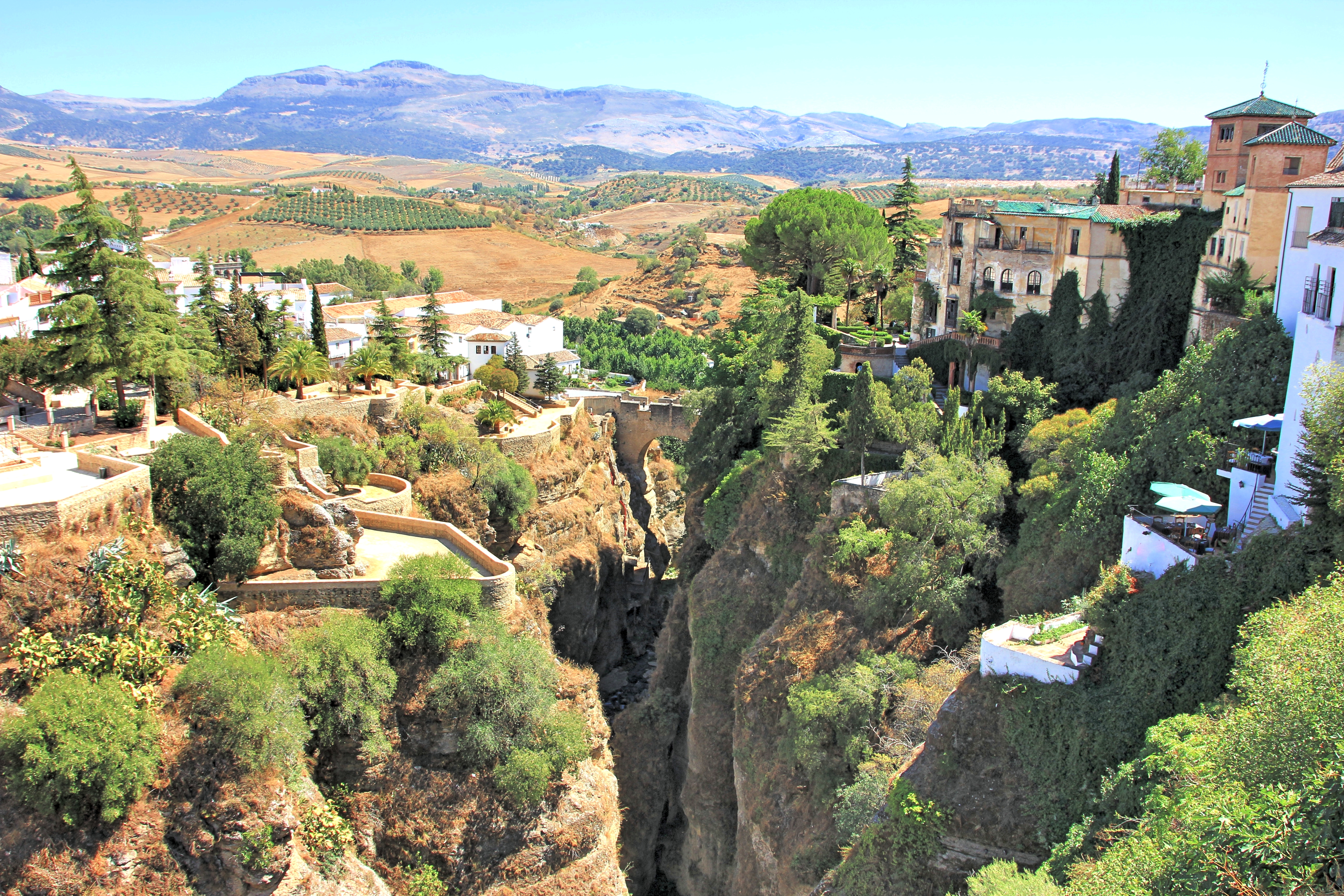 Deep stone gorge with houses on either side and greenery of trees dotted about at Ronda in Andalusia