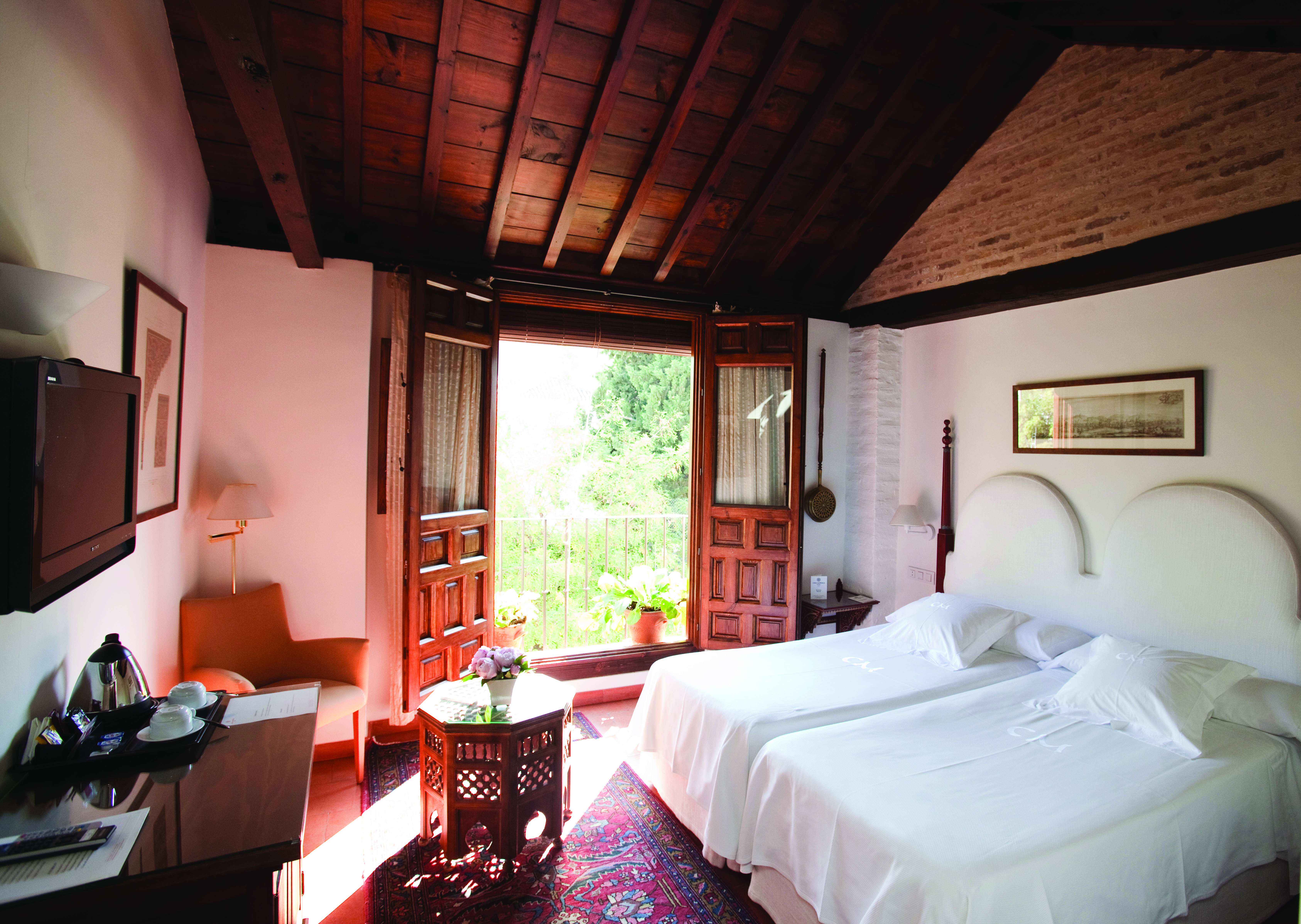 Standard room at the Casa Morisca with a double bed, television and double wooden doors leading onto a balcony