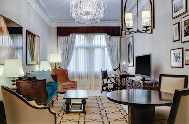 Executive suite living room with large crystal chandelier, television, draping curtains and velvet armchairs
