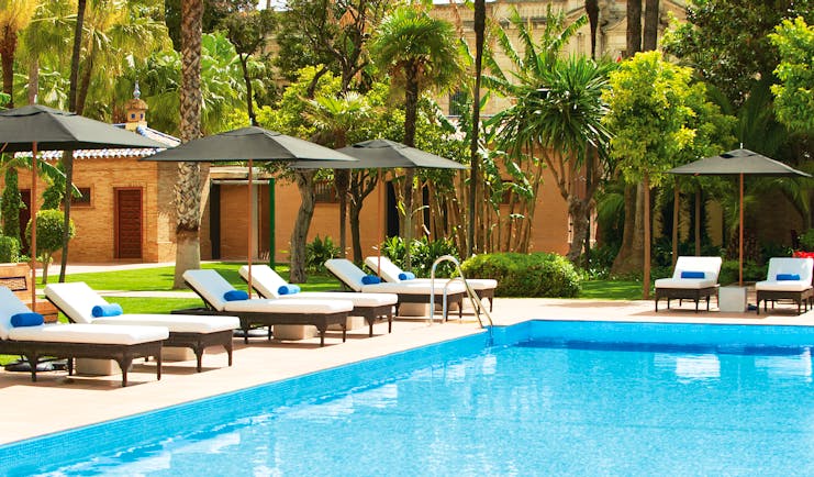 Outdoor swimming pool with trees and sun loungers surrouding the pool