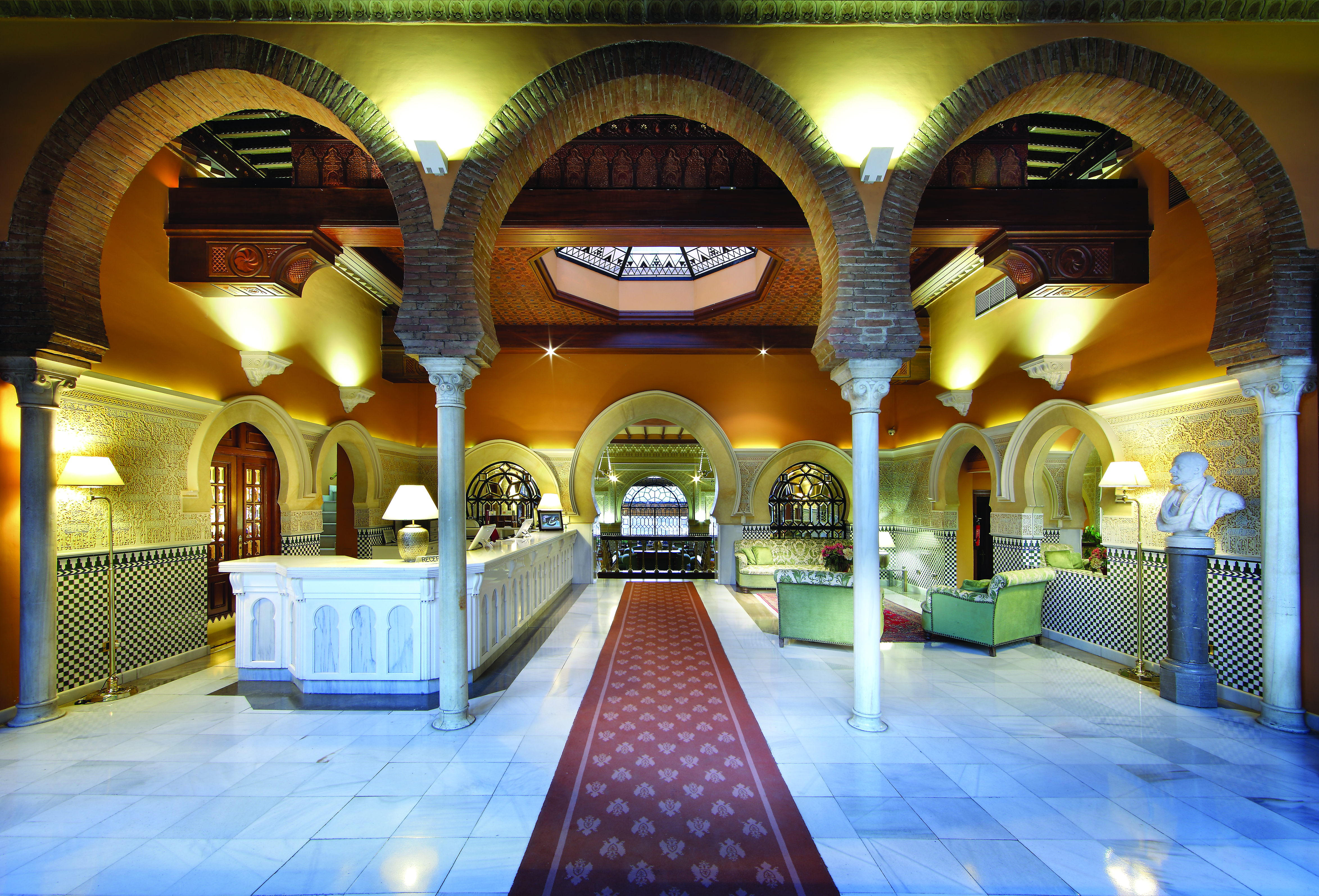 Reception at the Hotel Alhambra Palace with large archways with pillars and green seating areas 