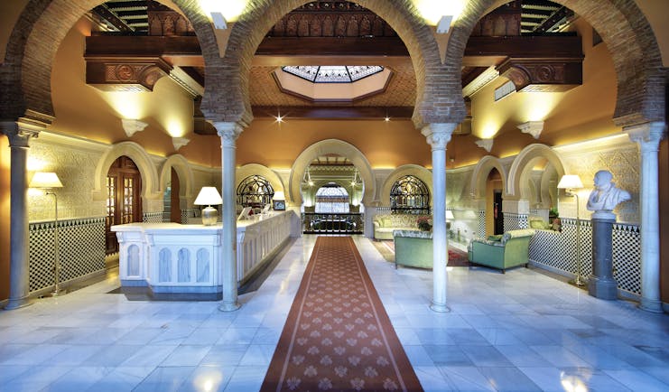 Reception at the Hotel Alhambra Palace with large archways with pillars and green seating areas 