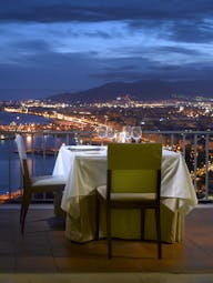 Parador de Malaga Gibralfaro dining terrace, table set for two, balcony overlooking the coast, town and mountain at night