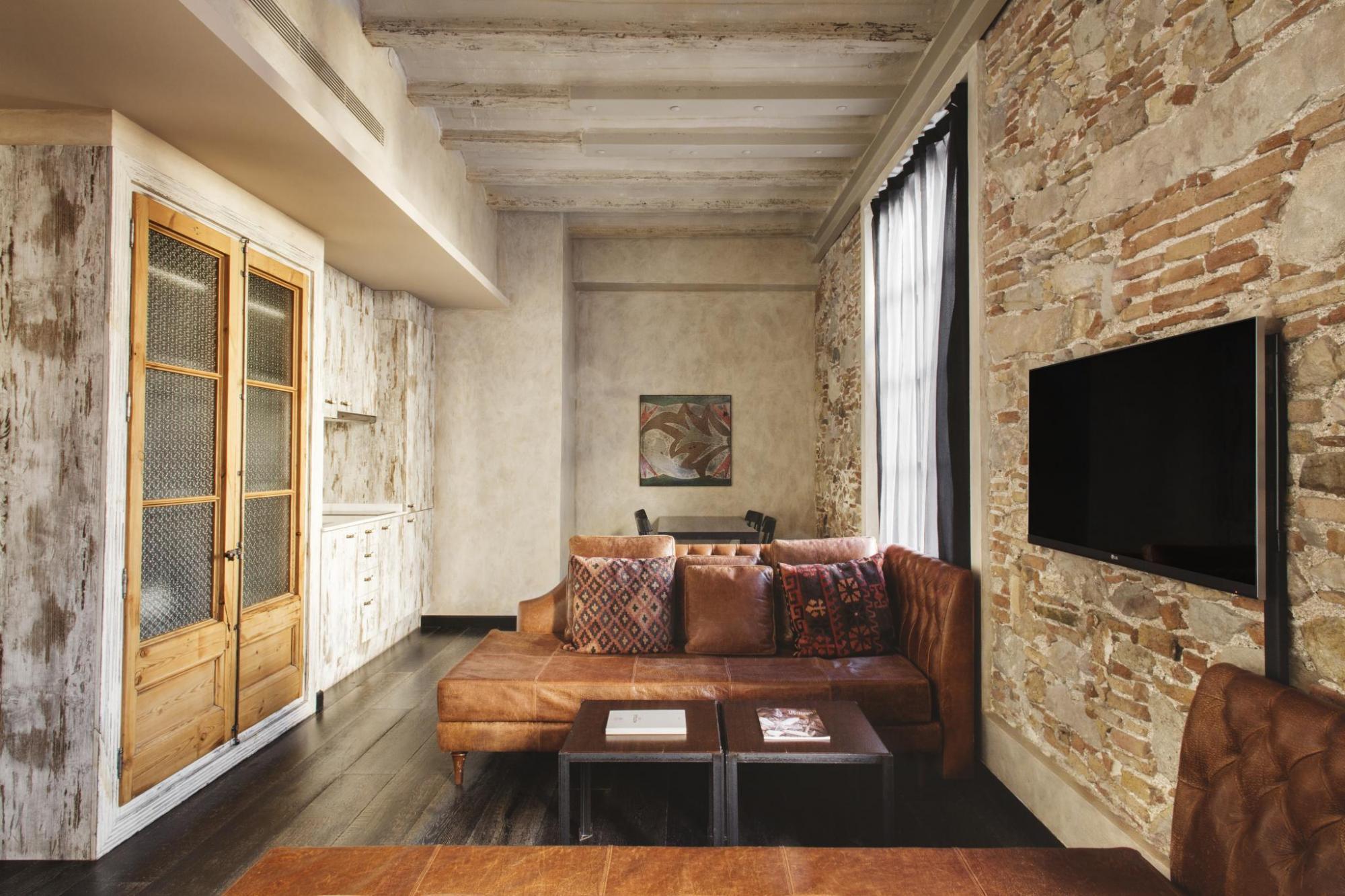 Hotel Arai Family Room with brown leather sofas, tv, stone walls, wooden beamed white ceiling, and light wood doors