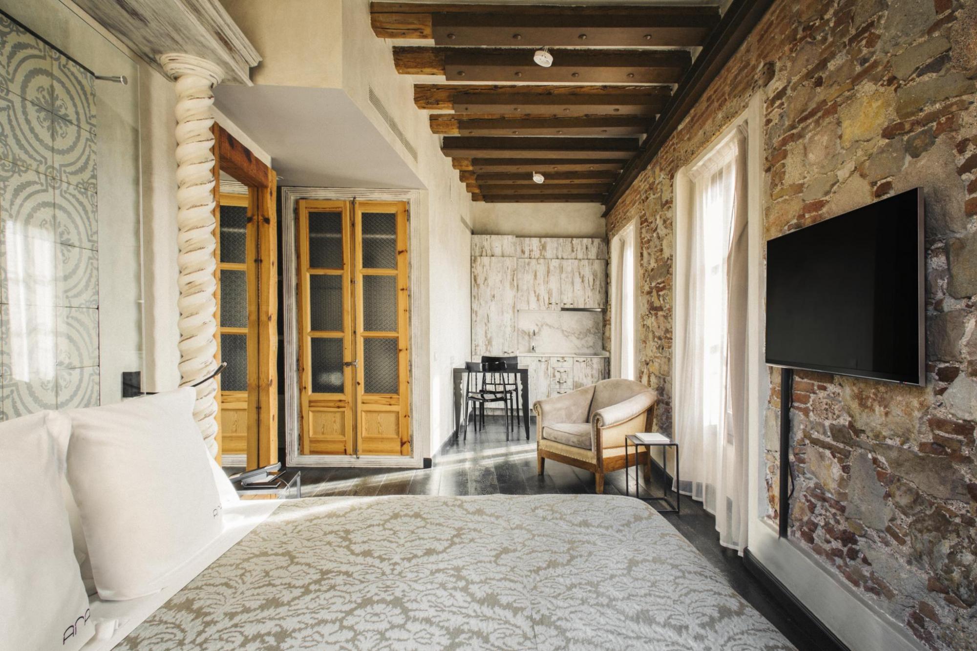 Hotel Arai Superior Room with exposed stone walls, large bed with neutral patterned bedding, wooden-framed doors, and beamed ceilingq