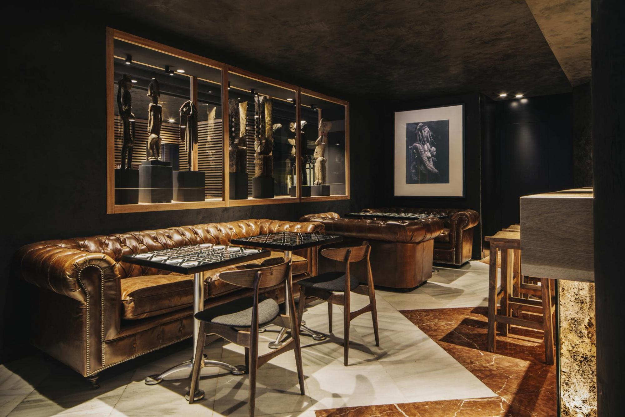 Hotel Balmes bar, with plush leather sofas, dark colour scheme, vintage artwork, and wooden chairs on marble floor