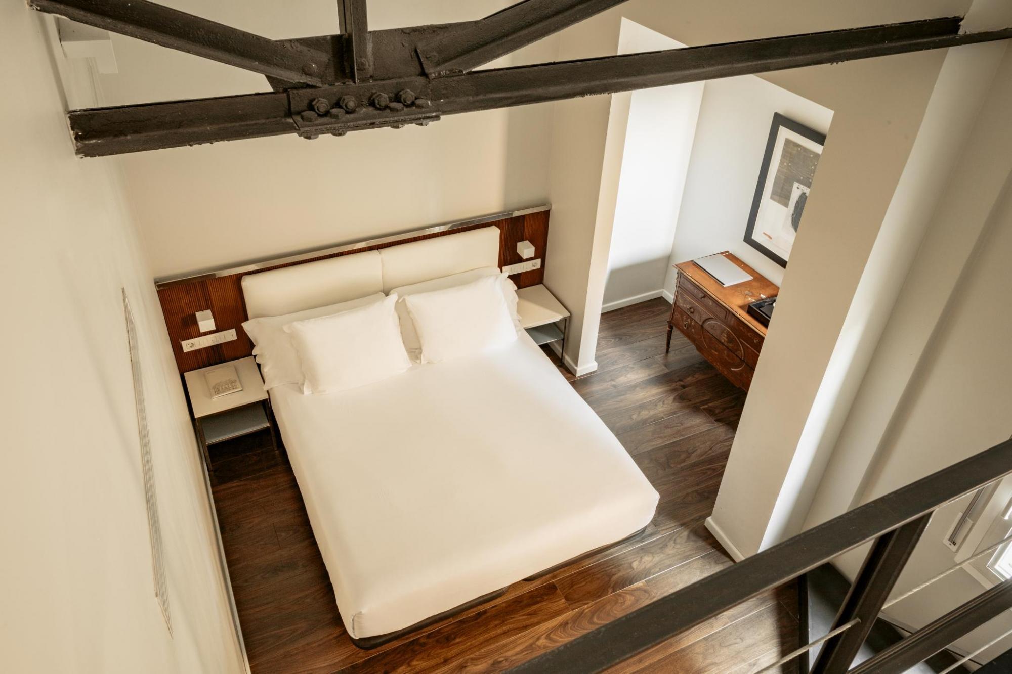 Hotel Balmes Premium Room, seen from above on a mezzanine level, looking down on the double bed with white linens, wooden floors, and desk alcove