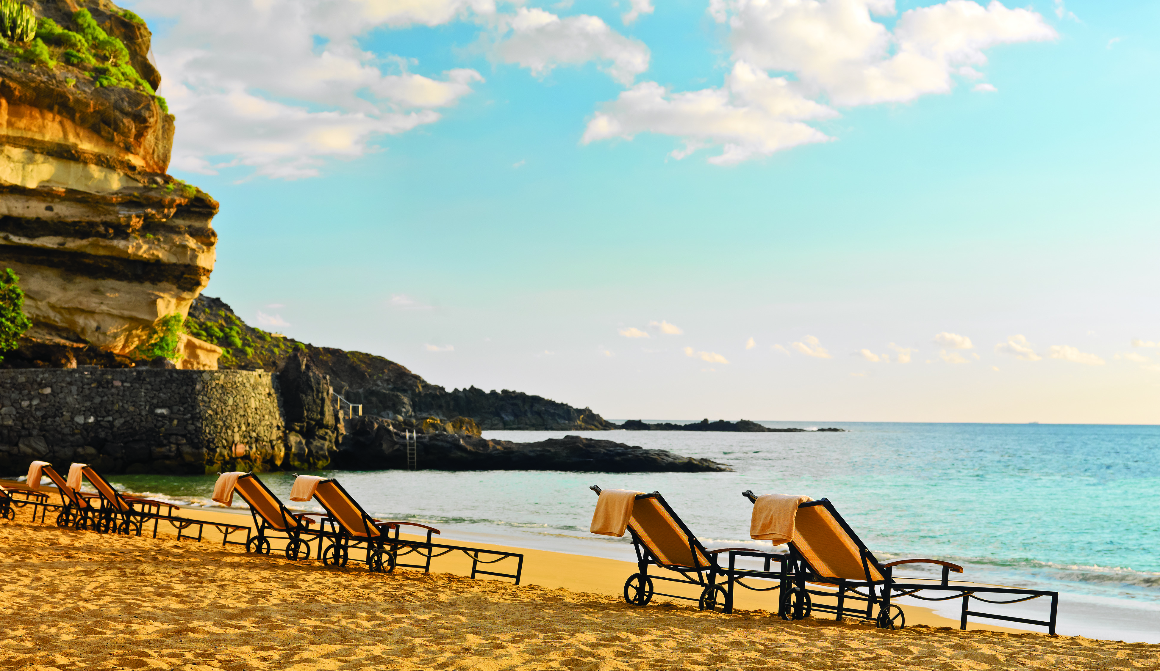 Beach with sun loungers on the sand and cliffs nearby