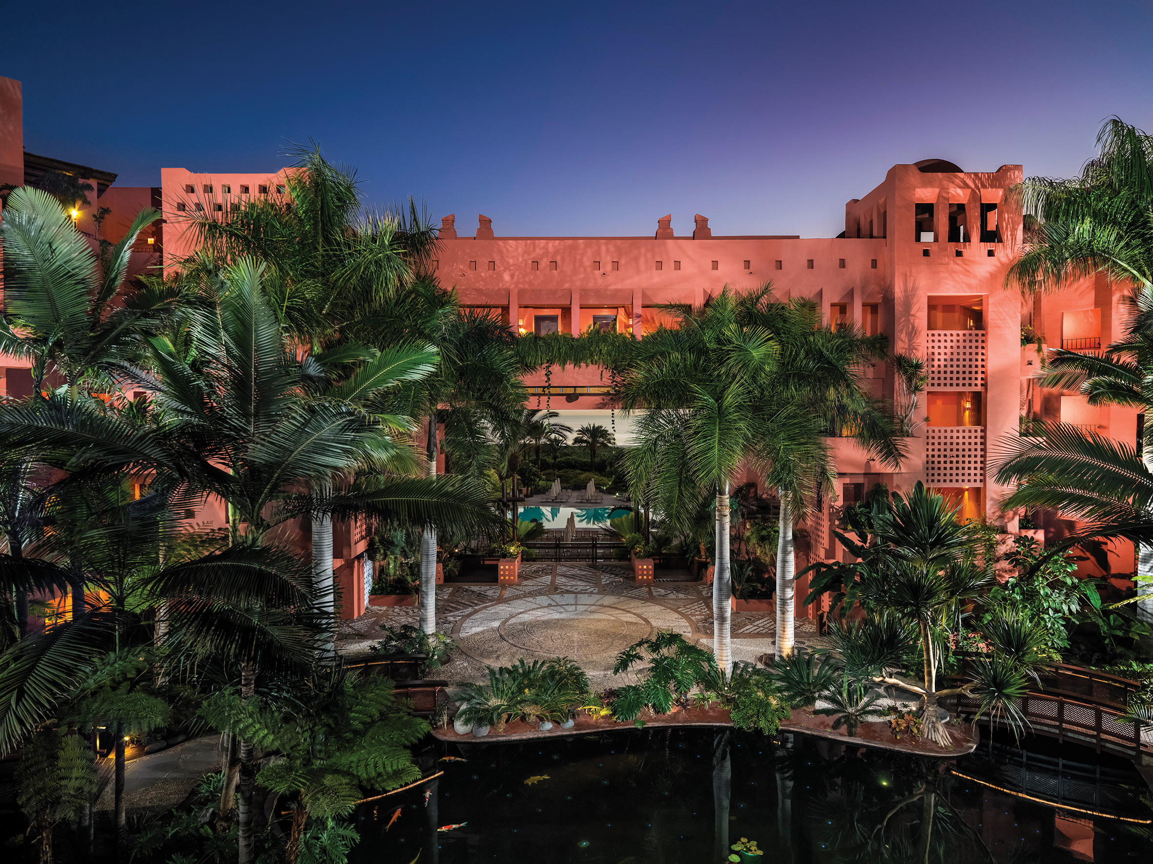 Exterior of hotel at night with palm trees covering the pink hotel building