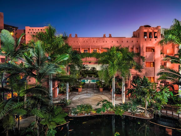 Exterior of hotel at night with palm trees covering the pink hotel building