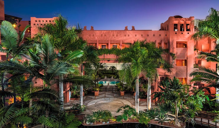 Exterior of hotel at night with palm trees covering the pink hotel building