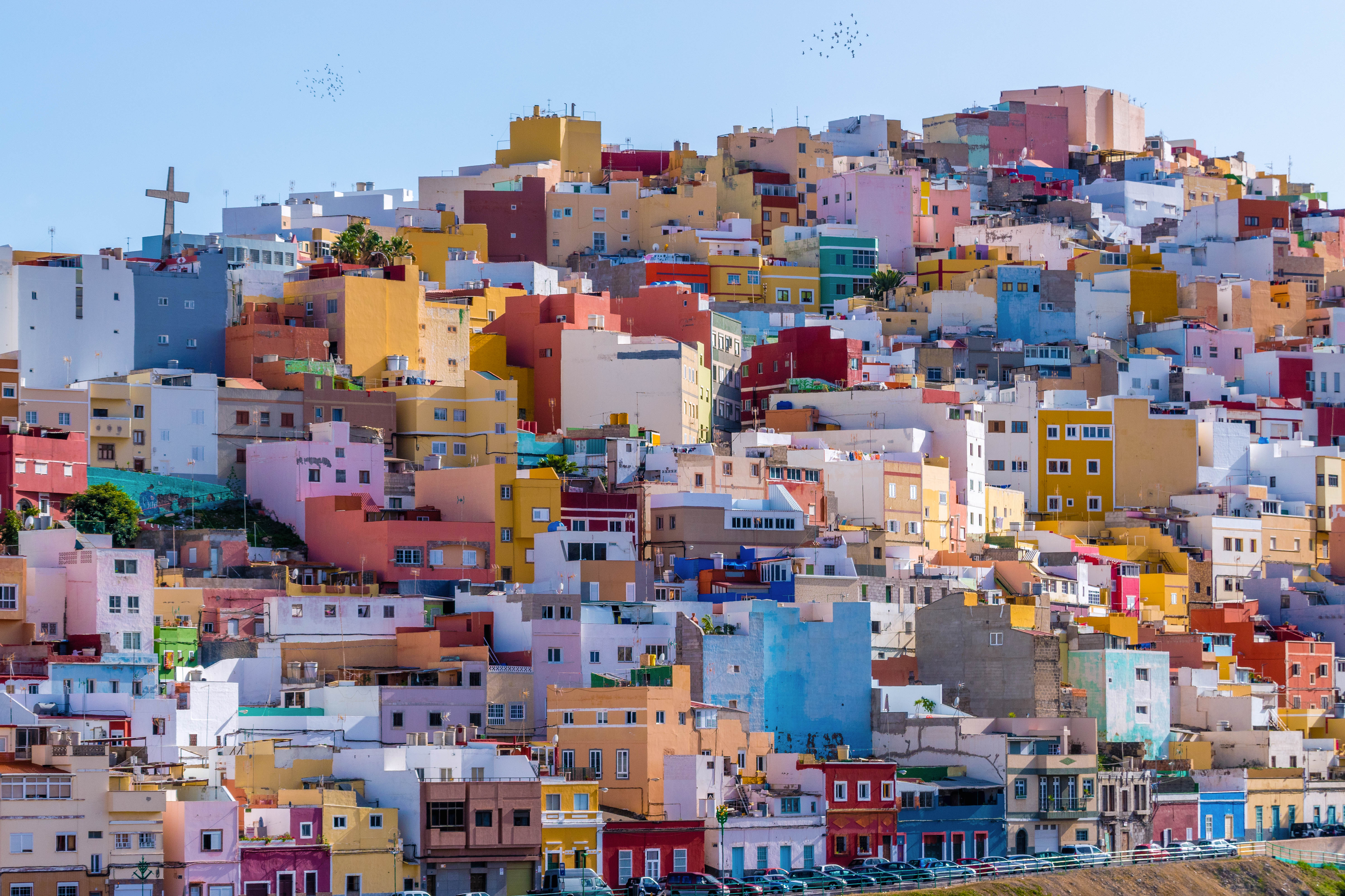 Brightly coloured houses of reds, pinks, blues and yellow on hillside with cross in sky in San Juan Las Palmas on Gran Canaria