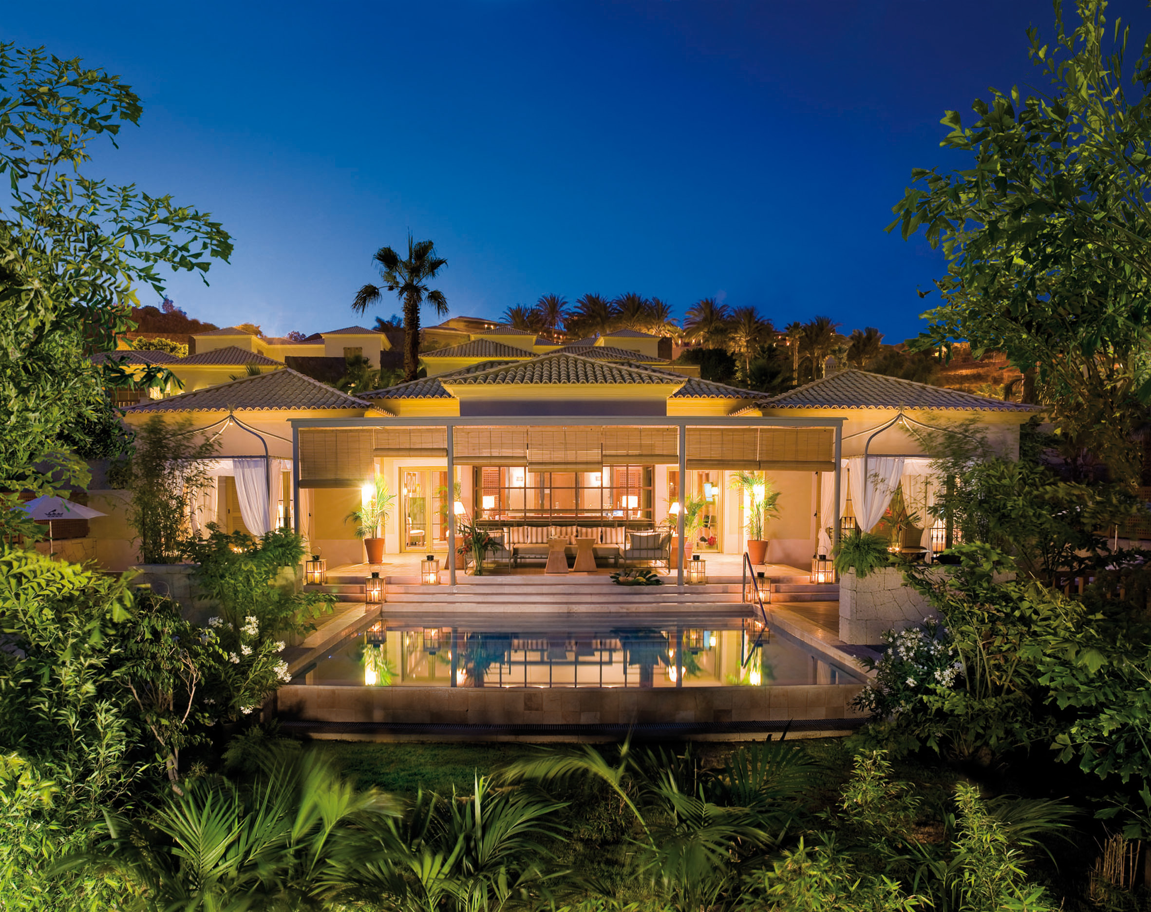 Exterior of  hotel lit up at night with greenery surrounding