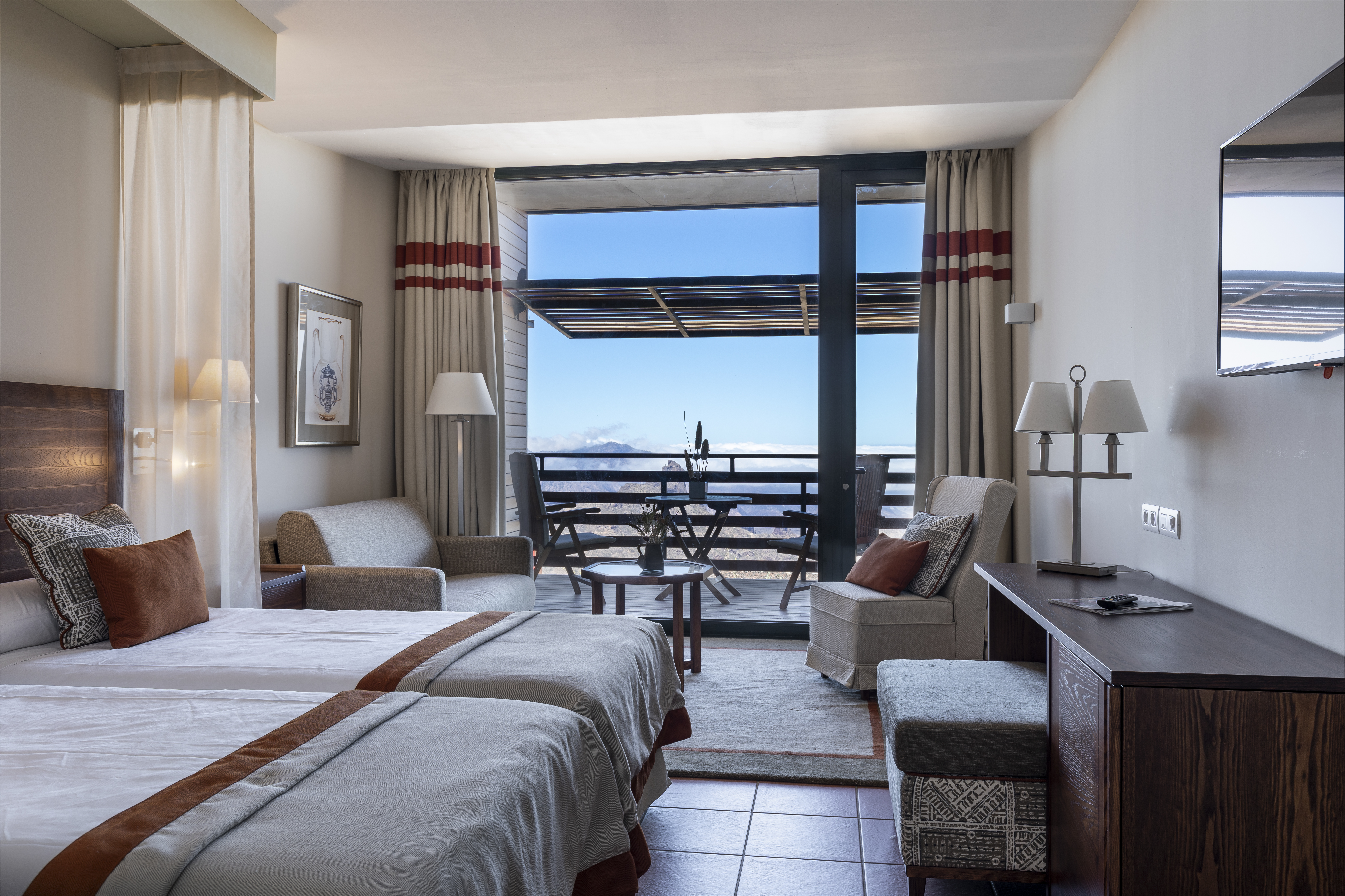 Standard double bedroom with two double beds, flatscreen television, sofas and chairs and bi-folding doors opening up onto a balcony